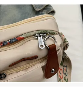 Detail of light beige nylon bag featuring multiple zippers and floral embroidered strap