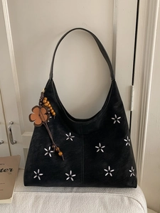 Grand cabas noir à broderie florale blanche avec breloque vintage sur un canapé