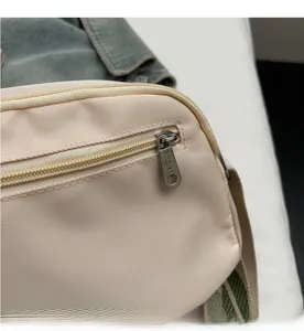 Close-up of smooth metal zipper detail on beige nylon crossbody bag with fabric texture