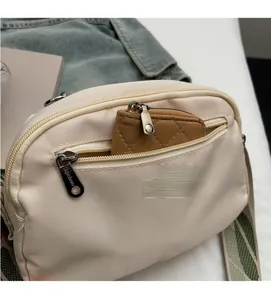 Detail of beige nylon crossbody bag showing spacious front zipper pocket and brown coin purse