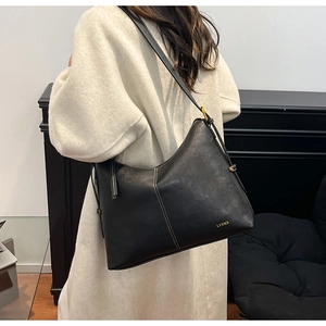 Detail showing the white stitching and gold foil brand logo on black leather tote bag