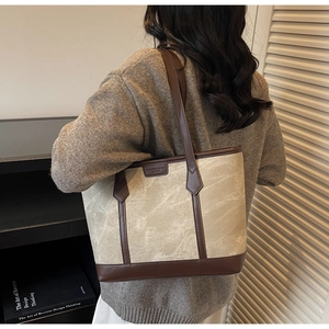 Detail einer beige marmorierten Canvas-Einkaufstasche mit dunkelbraunen Ledergriffen am Modell