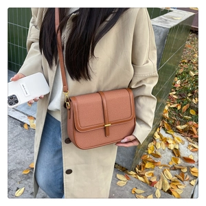 Detail of brown woven textured crossbody bag with gold buckle in an outdoor lifestyle setting