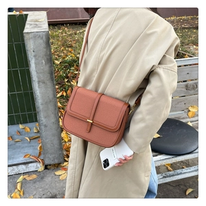 Detail view of brown pebbled leather shoulder bag with gold clasp shown in outdoor setting