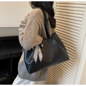 Detail of a large black matte leather tote bag with a printed silk scarf on a model