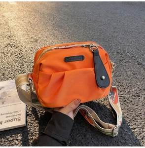 Detail of bright orange nylon crossbody bag with multi-pockets and patterned wide strap