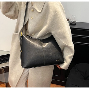 Detail of black underarm bag with white stitching and gold logo on beige coat