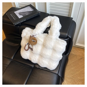 Détail d'un sac cabas blanc en fausse fourrure avec breloque peluche sur un banc en cuir noir