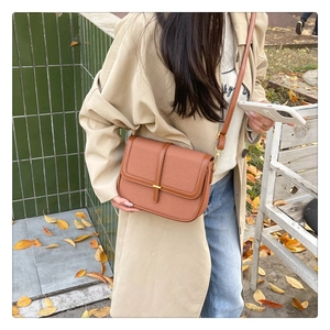 Outdoor shot of caramel textured crossbody bag with gold metal buckle and leather strap