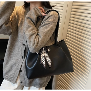 Detail of a black leather tote bag with a geometric pattern scarf on the shoulder strap