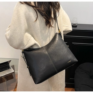 Detail of black leather tote bag featuring white cross-stitching and gold logo on surface