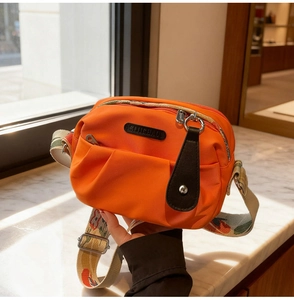Detail of orange nylon crossbody bag with multi-zipper pockets and ethnic printed strap