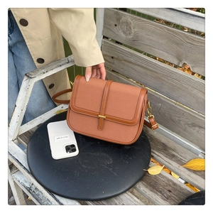 Close-up of a brown canvas and leather shoulder bag with gold clasp on an autumn bench