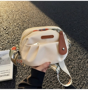 Close-up of beige ruched crossbody bag with embroidered floral strap and leather logo