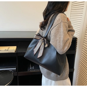 Close-up of a black leather tote bag featuring a decorative black and white wavy silk scarf