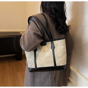 Minimalistische beige Shopper-Tasche mit schwarzem Lederbesatz, über der Schulter getragen