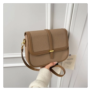 Close-up of brown textured woven flap bag with gold clasp and leather trim details