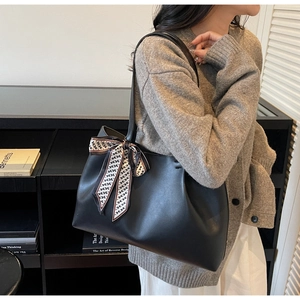 Close-up of black leather tote bag featuring a chic H-print silk scarf tied on the handle