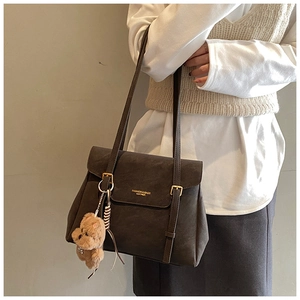 Détail d'un cabas en cuir marron foncé avec boucle dorée et ours en peluche sur modèle