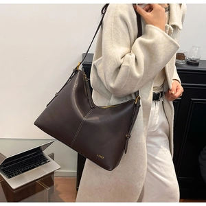 Detail of dark brown leather tote bag with white stitching and metal zipper on model
