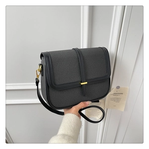 Detailed close-up of dark grey square crossbody bag with gold clasp and black leather trim