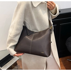 Detail of dark brown leather tote bag with white stitching and luxury metal logo