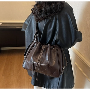 Détail du sac seau marron foncé avec cordons, motif matelassé et fermeture éclair argent