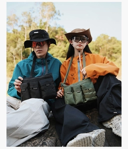 Outdoor utility shoulder bag with multi-pocket design shown on models in nature