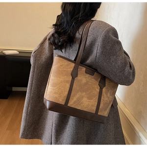 Detail einer großen braunen Tote-Bag mit Marmormuster, getragen über einem grauen Blazer