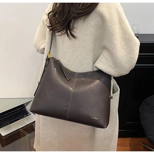 Detail of dark brown matte leather tote bag featuring a brand logo and long shoulder strap