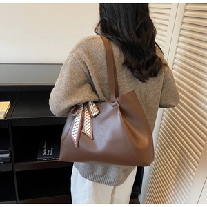 Brown leather tote bag with a decorative geometric scarf handle in a cozy room setting