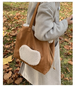 Detail of a brown suede tote bag with white faux shearling trim and a fuzzy heart patch