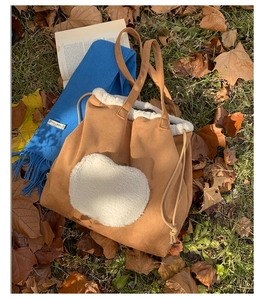 Detailed view of brown suede tote bag with white fleece heart on autumn leaves background