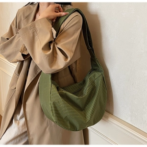 Dettaglio della borsa a tracolla a quadretti verdi indossata con un trench kaki casual