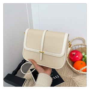 Detail of minimalist beige canvas and white leather handbag with gold metal clasp on a chair