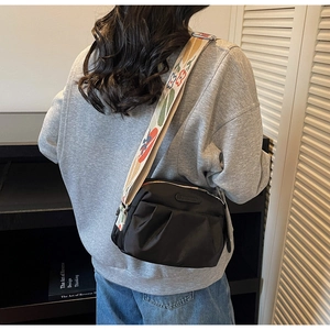Detail of black pleated crossbody bag with a colorful embroidered wide shoulder strap