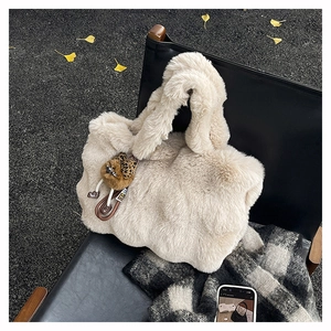 Détails d'un sac cabas en peluche beige avec un charm léopard sur une chaise en cuir