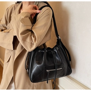 Détail d'un sac seau noir matelassé avec cordon de serrage et poche zippée sur modèle