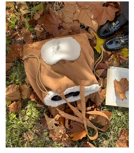 Close-up of brown suede tote bag with white faux fur trim and drawstring on autumn leaves