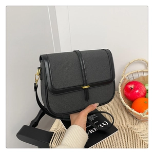 Close-up of black textured fabric shoulder bag with gold metal buckle and flap design