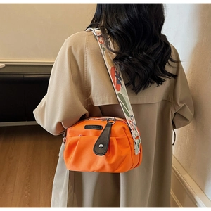 Detail of orange ruched crossbody bag with colorful embroidered floral shoulder strap