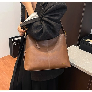 Deep brown leather tote bag with gold hardware worn by a model in a modern office setting