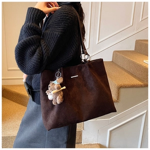 Detail of dark brown quilted tote bag with matte texture and cute plush bear charm