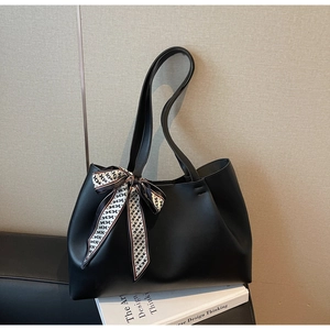 Detail view of large black tote bag with decorative H-pattern silk scarf on a leather chair