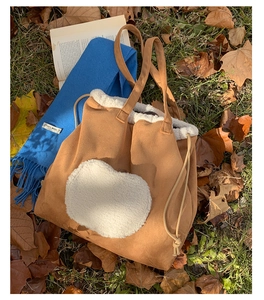 Detail of a brown suede tote bag with white faux fur heart patch on autumn grass