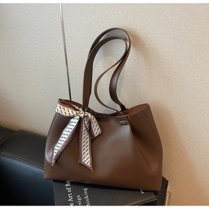 Close-up of dark brown leather tote bag with elegant H-pattern silk scarf on handle