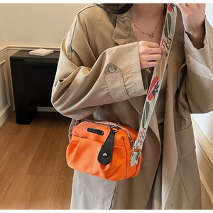 Detail of orange pleated nylon crossbody bag with floral pattern wide strap on model