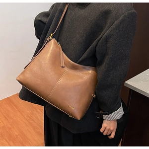 Detailed close-up of brown leather tote bag showing adjustable strap and brand logo