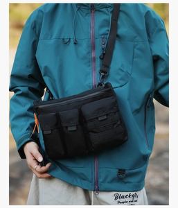 Detail of black tactical crossbody bag with multiple pockets and orange cord accents