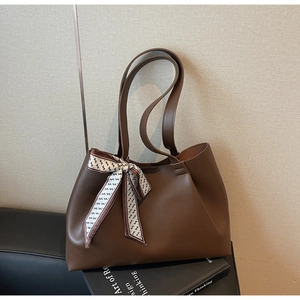 Detail of dark brown tote bag on books featuring a decorative geometric silk scarf knot